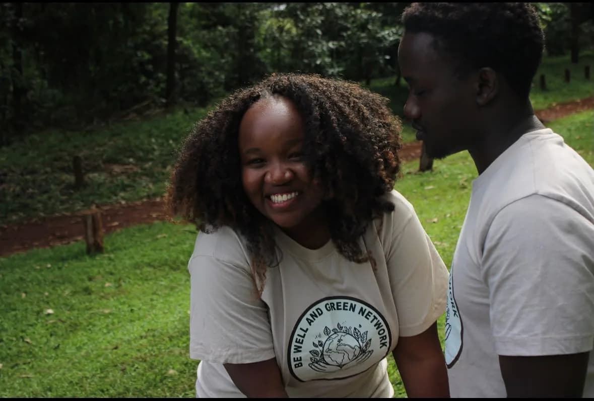 Two smiling BWGN volunteers in branded T-shirts outdoors among trees